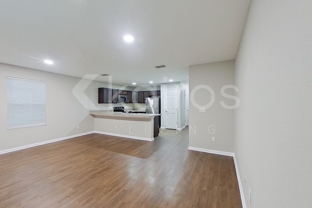 A spacious room with wooden flooring and a kitchen area in the background.