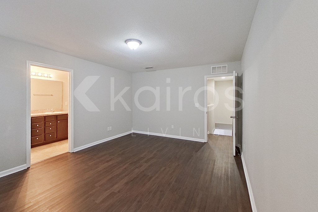 A room with wooden floors and white walls, with a doorway leading to another room.