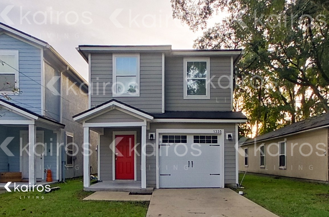 A house with a red door is in front of a tree and other houses.
