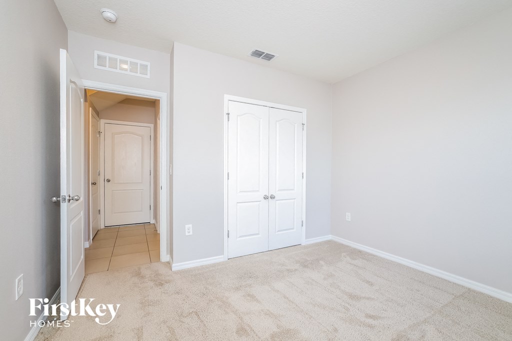 A white bedroom with a carpeted floor and two doors.