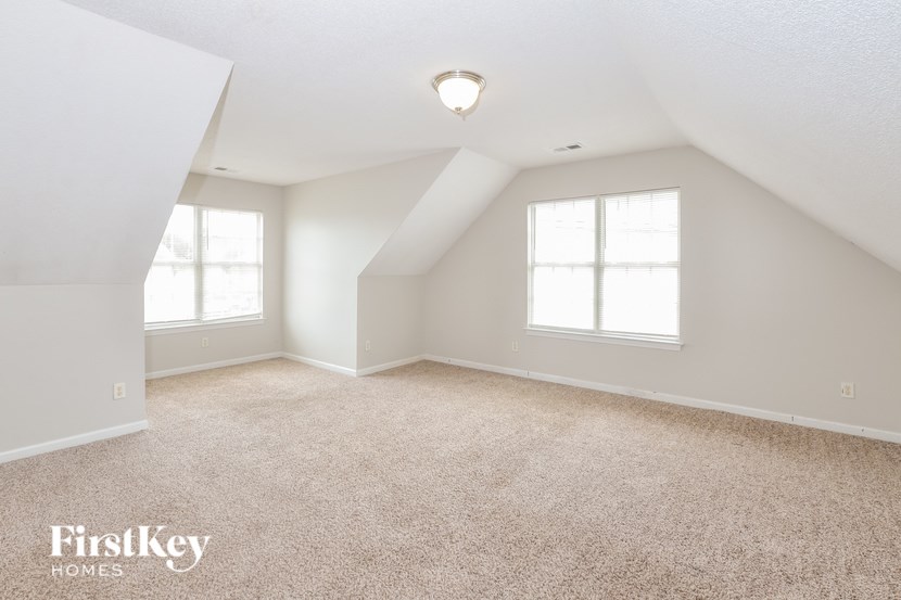 A spacious room with a carpeted floor and two windows.