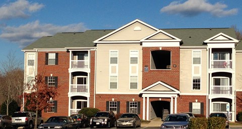 A large brick building with a green roof and a parking lot in front.