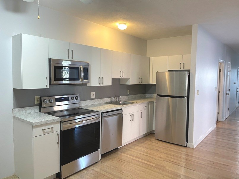 an empty kitchen with stainless steel appliances and white cabinets