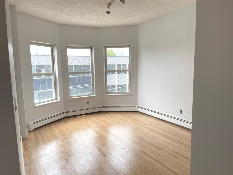an empty living room with a hardwood floor and three windows