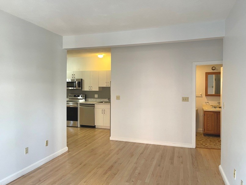 an empty living room with a kitchen in the background