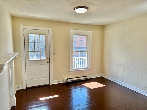 A room with a white door and a window with a view of a red building.