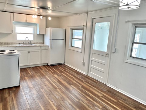 A kitchen with a white fridge and wooden floors.