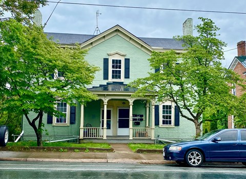 A blue car is parked in front of a green house.