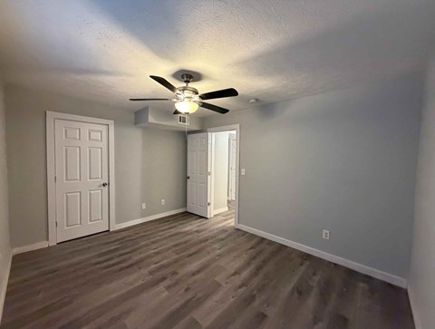A room with a ceiling fan and light fixture, two doors, and a wooden floor.