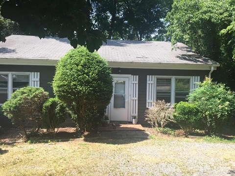 a small house with a white door and a yard with bushes