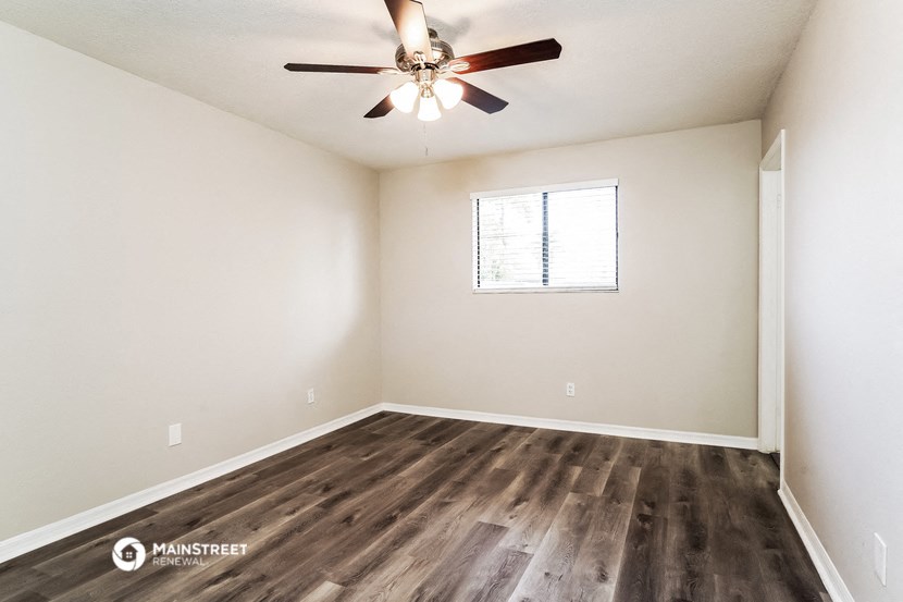 the spacious living room with wood flooring and a ceiling fan