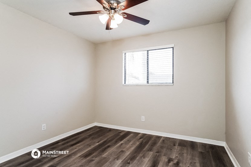 the spacious living room with wood flooring and a ceiling fan