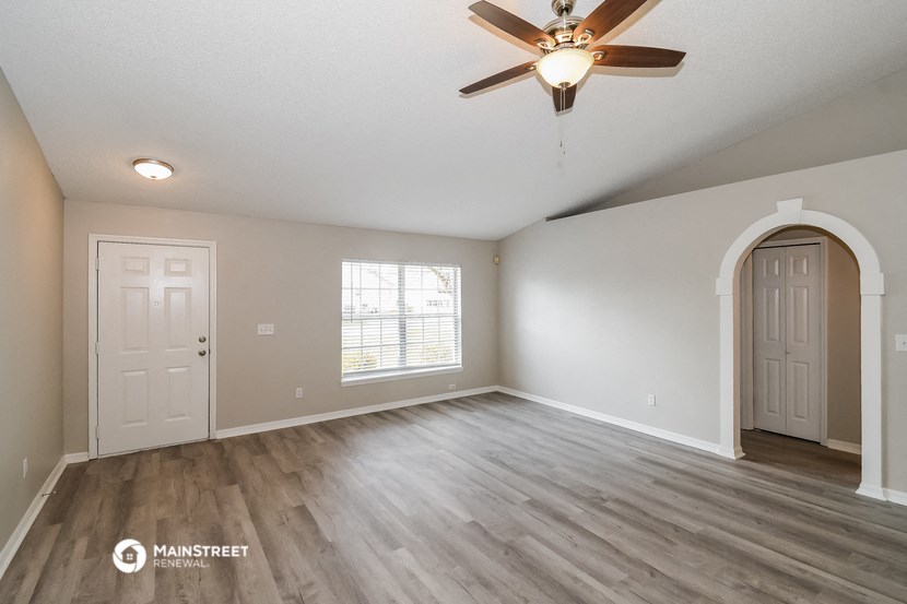 the spacious living room with hardwood flooring and a ceiling fan
