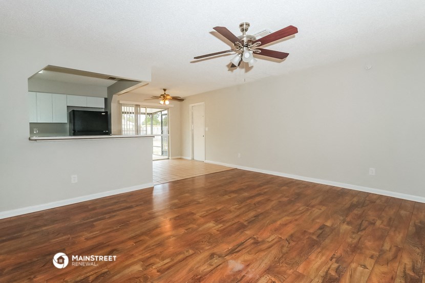 an empty living room with a ceiling fan and a kitchen