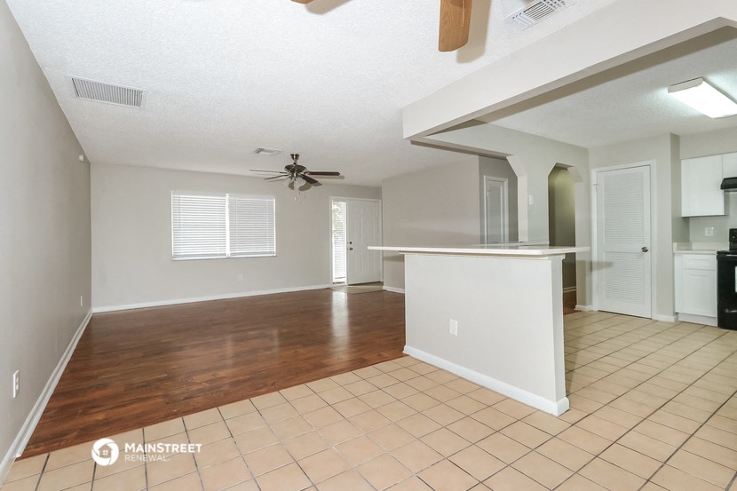 an empty living room with a kitchen and a ceiling fan
