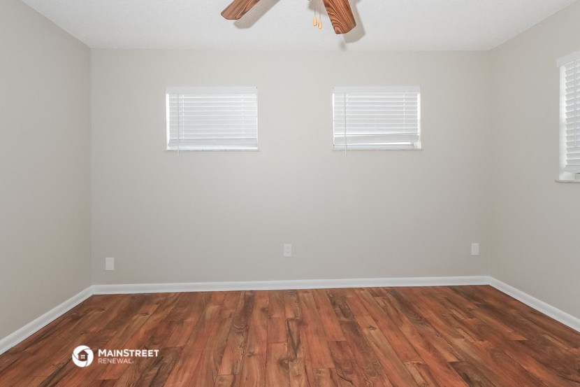 a room with wooden floors and two windows and a ceiling fan