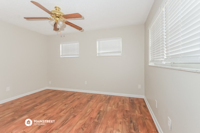 the spacious living room with hardwood flooring and a ceiling fan
