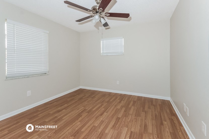 the spacious living room with hardwood flooring and a ceiling fan