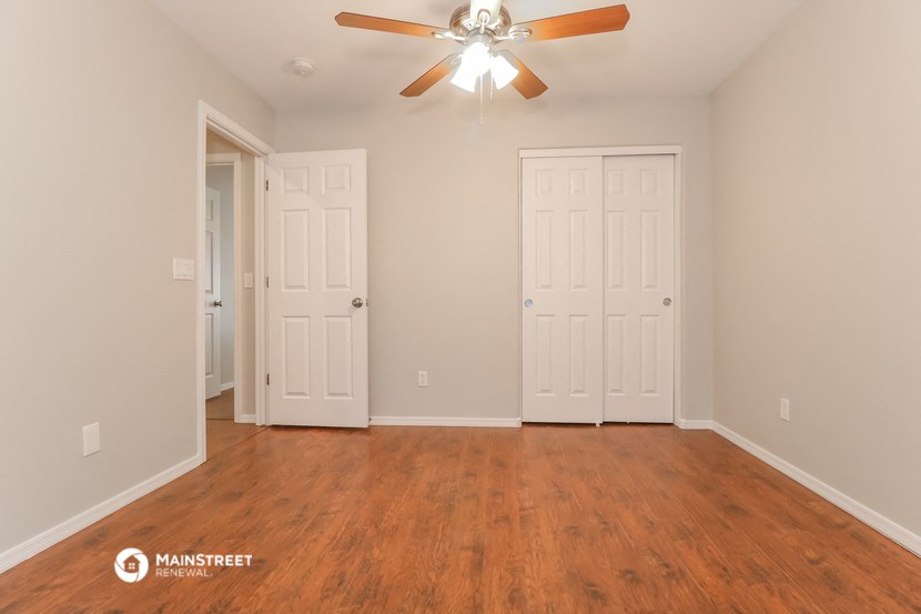 the spacious living room with two doors and a ceiling fan