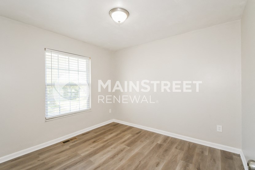 a bedroom with white walls and wood flooring and a window