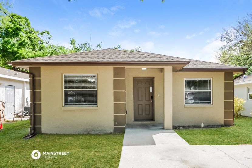 the front of a tan house with a sidewalk and grass
