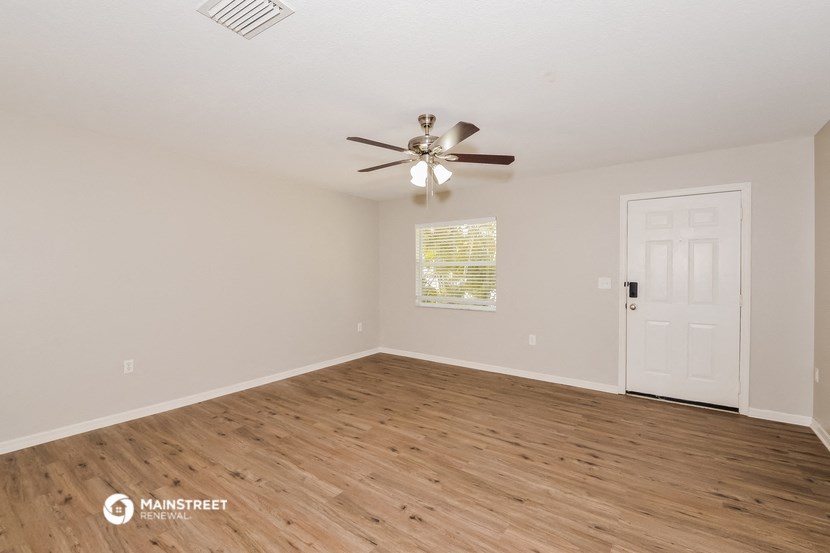 the spacious living room with wood flooring and a ceiling fan