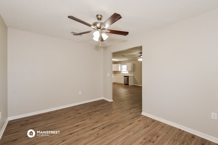the living room and dining room of an apartment with wood floors and a ceiling fan
