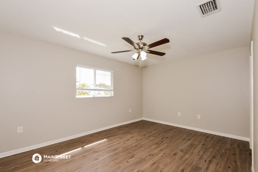 the spacious living room with wood flooring and a ceiling fan