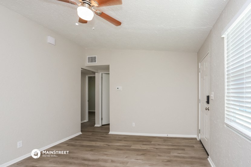 the spacious living room with a ceiling fan and white walls
