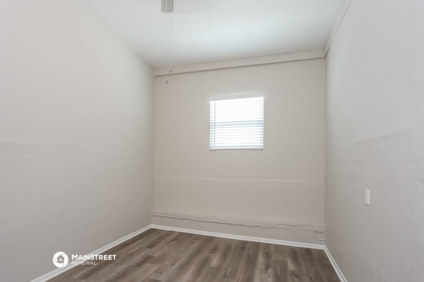 a bedroom with white walls and wood floors and a window