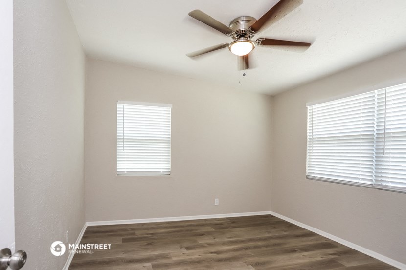 the spacious living room with a ceiling fan and two windows