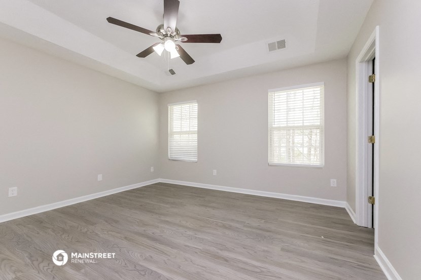 the spacious living room with hardwood flooring and a ceiling fan