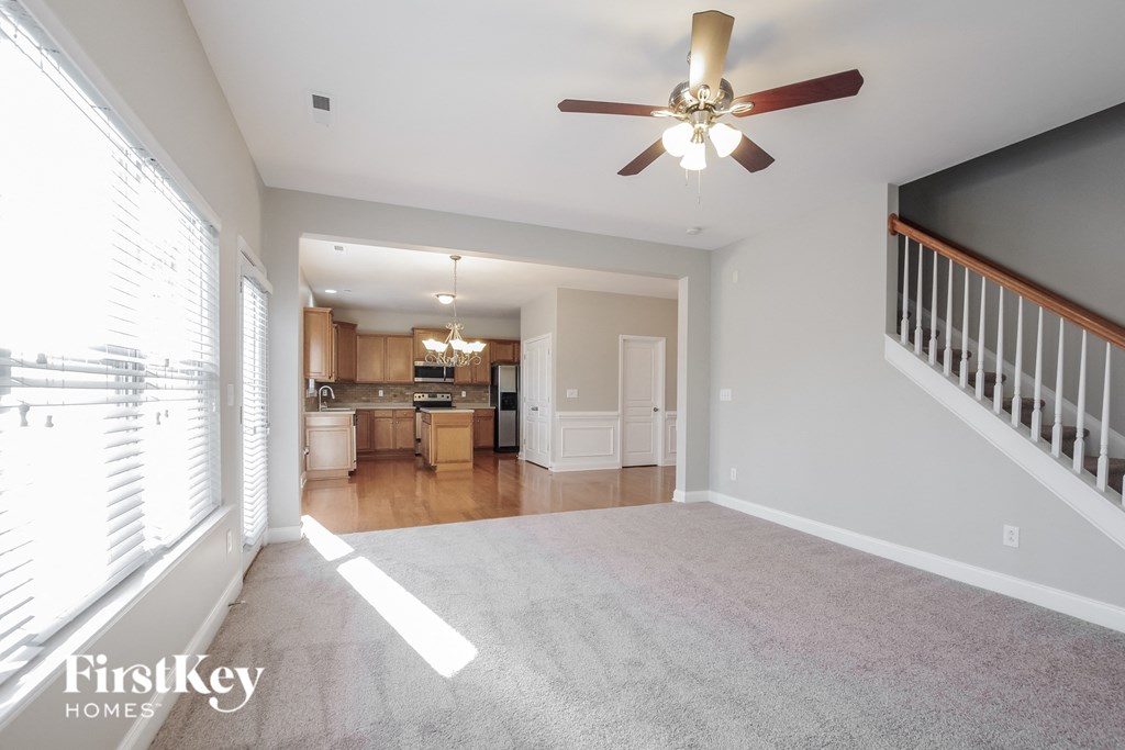 an empty living room with a ceiling fan and a kitchen