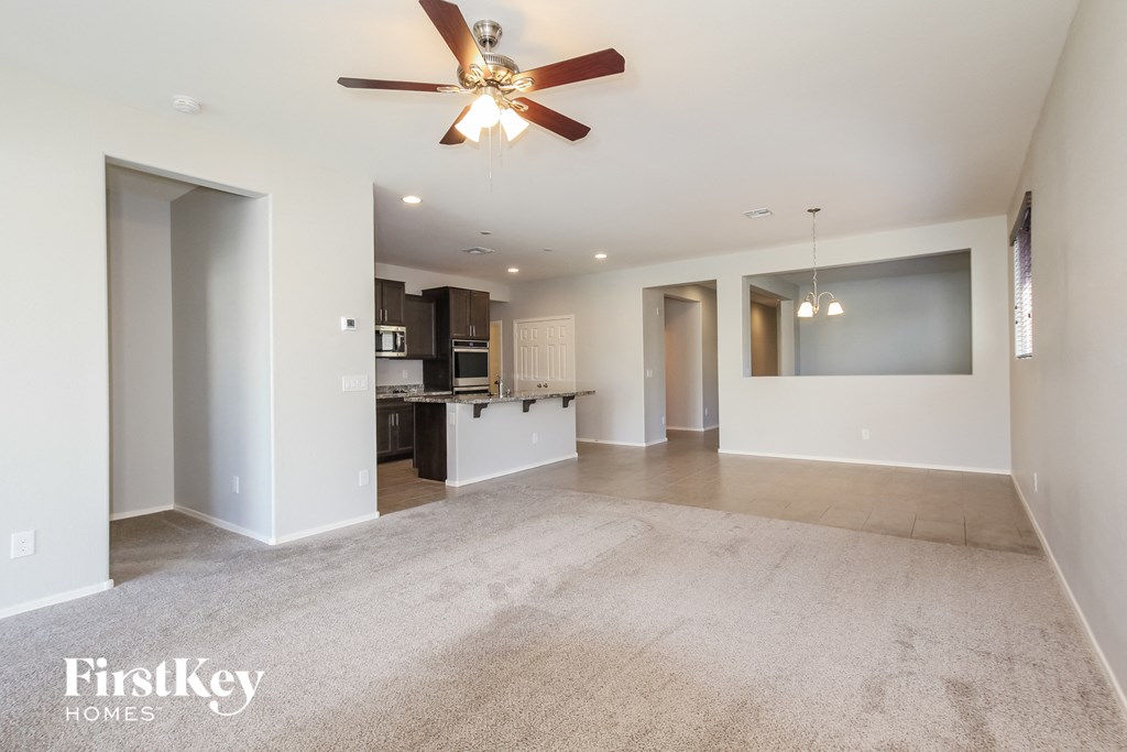 A spacious living room with a ceiling fan and a kitchen in the background.