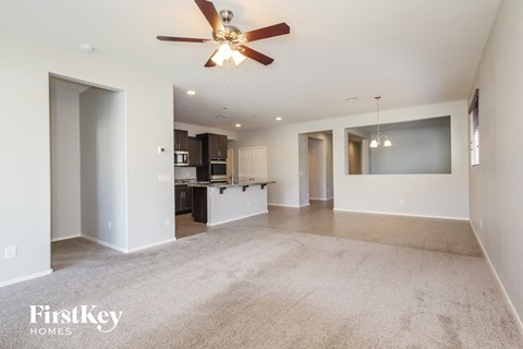 A spacious living room with a ceiling fan and a kitchen in the background.