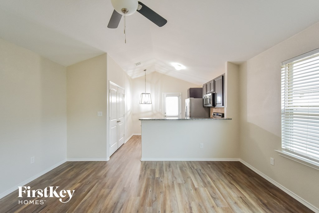 the living room and kitchen of an apartment with wood flooring and a ceiling fan