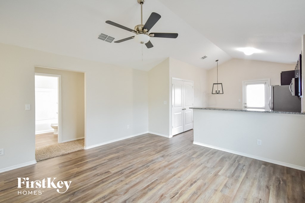an empty living room with a kitchen and a ceiling fan
