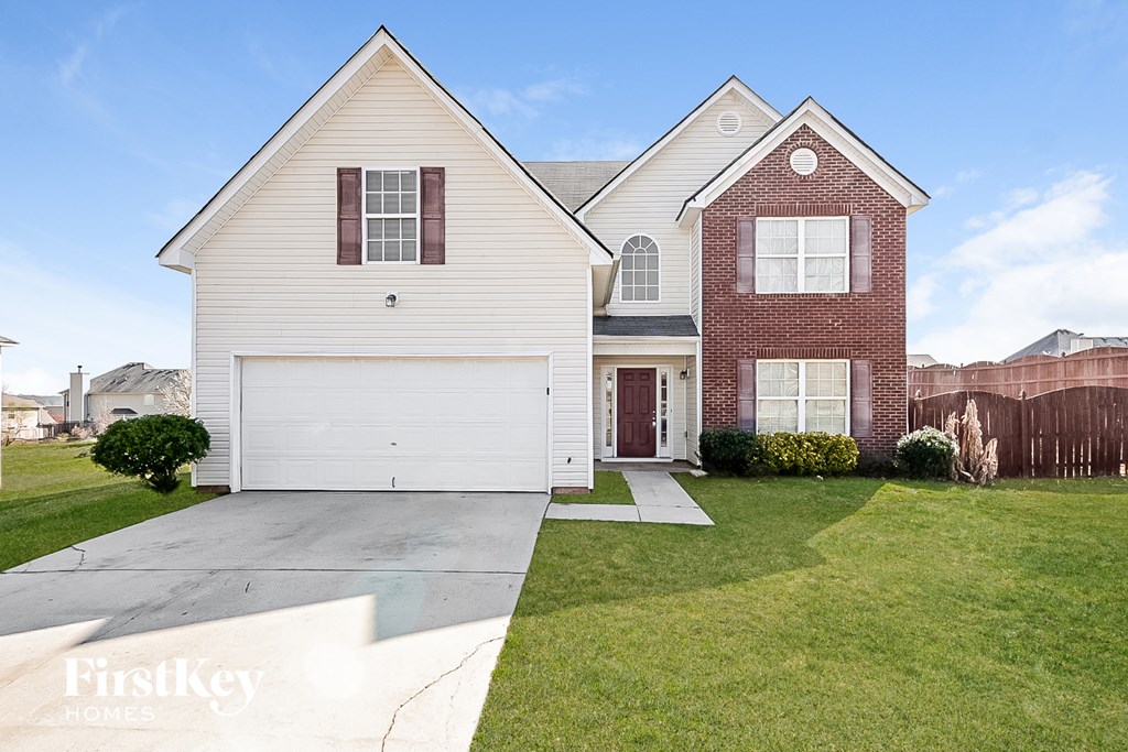 a white and brick house with a white garage door and a lawn
