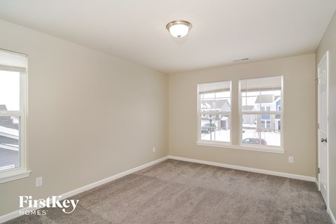 a spacious living room with carpet and two windows