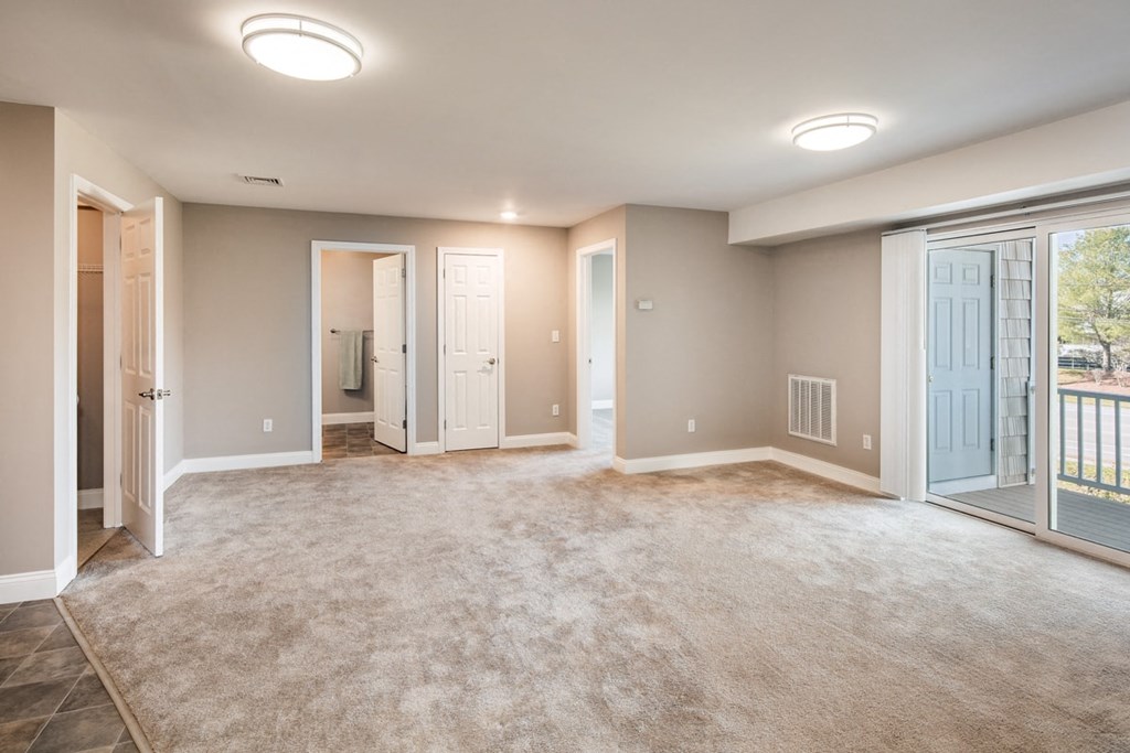 A spacious room with a carpeted floor and a balcony door.