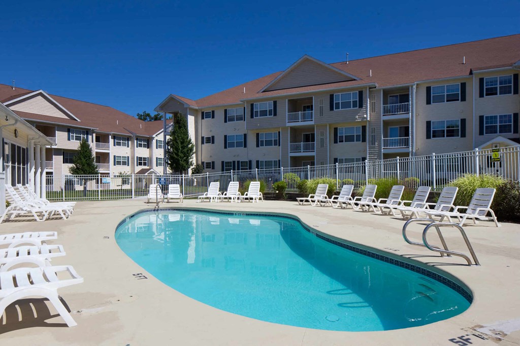 A swimming pool surrounded by sun loungers in front of a hotel.