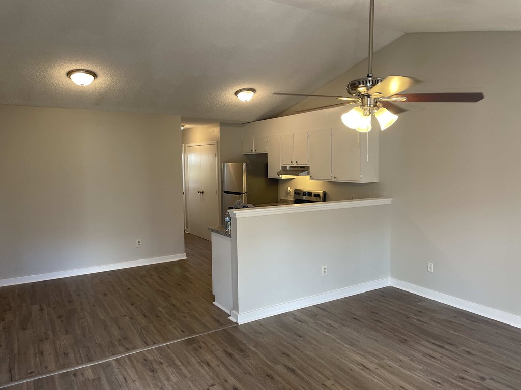 an empty living room with a kitchen and a ceiling fan