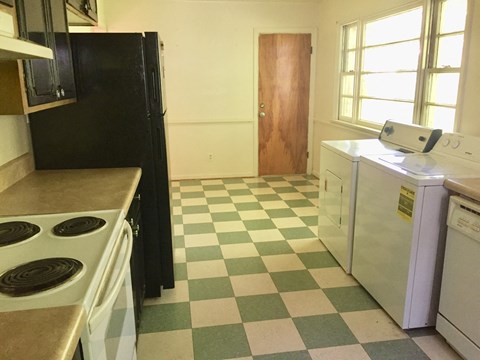 A black refrigerator sits in a kitchen with a checkered floor.
