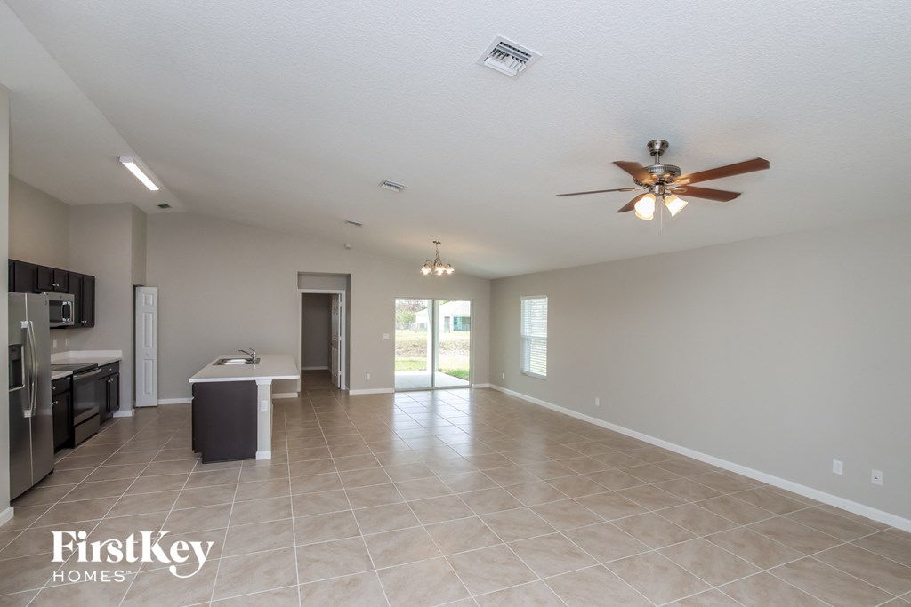 A spacious living room with a kitchen area in the background and a ceiling fan in the middle of the room.