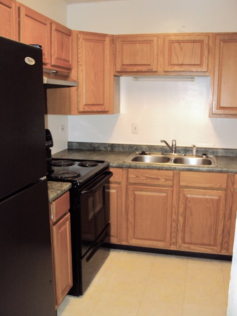 a kitchen with wooden cabinets and a black refrigerator and a sink