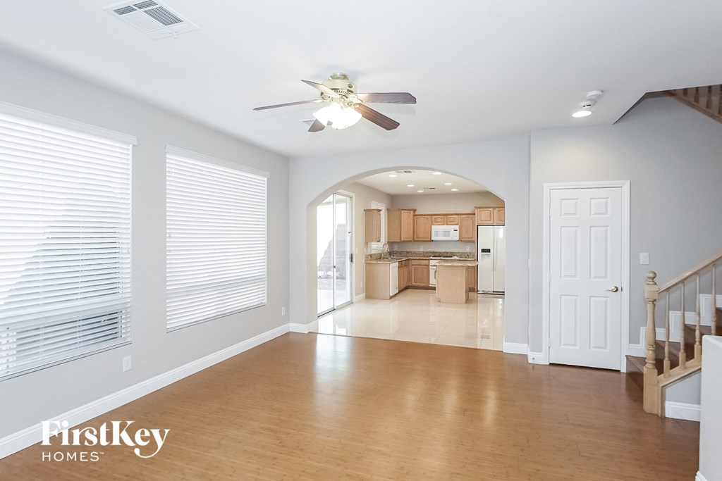 A spacious living room with a ceiling fan and a staircase.