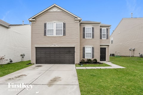 a tan house with a black garage door in front of a green lawn