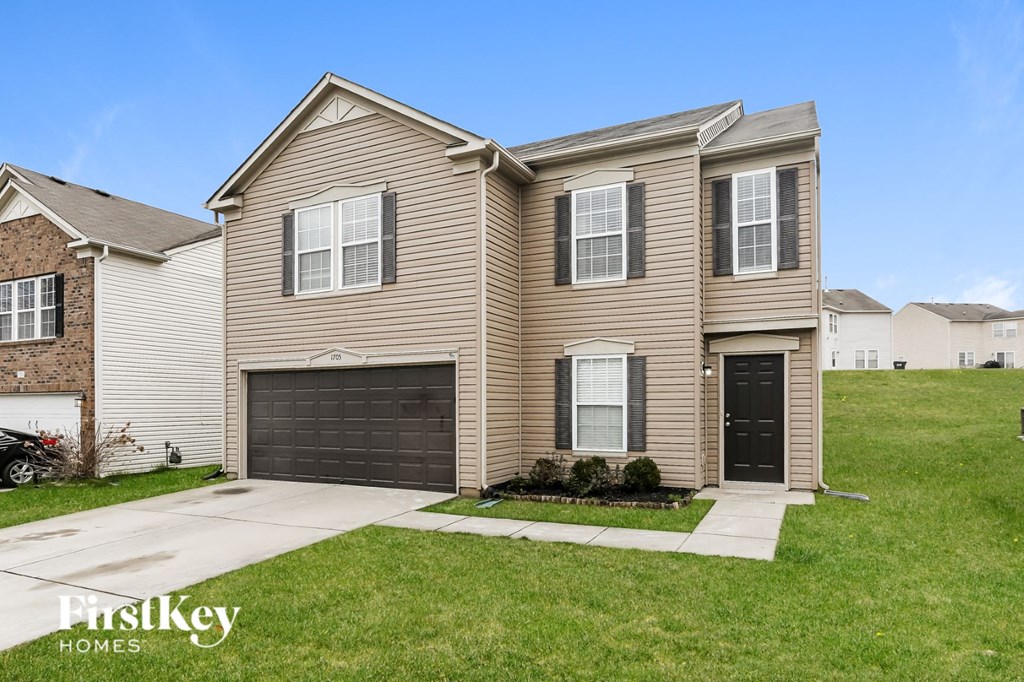 a tan house with a black garage door in front of a green lawn