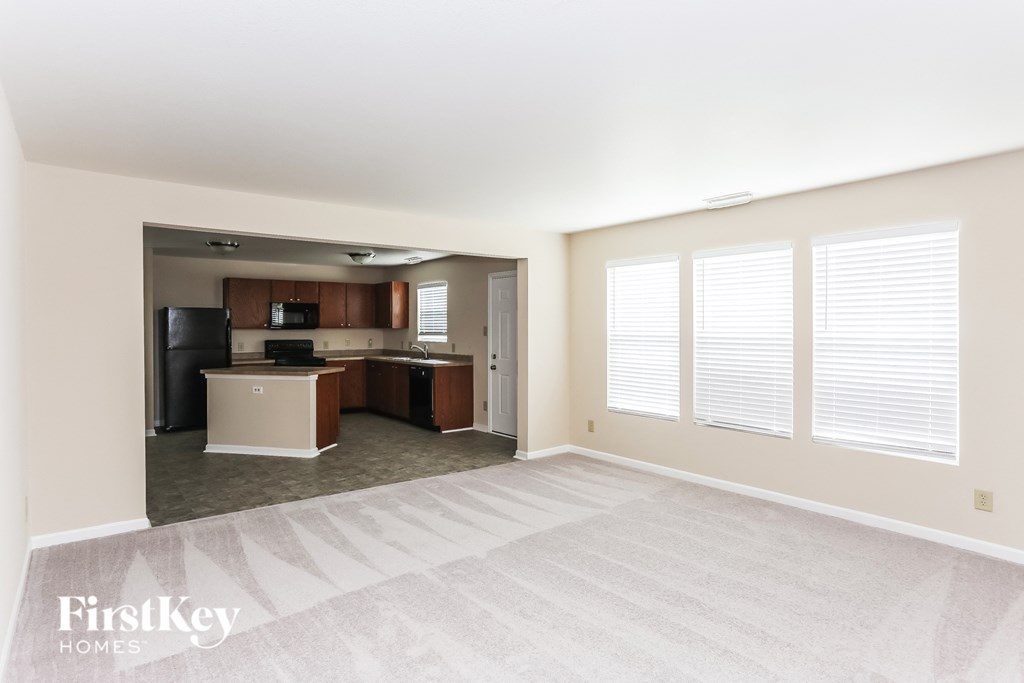 an empty living room with a kitchen in the background