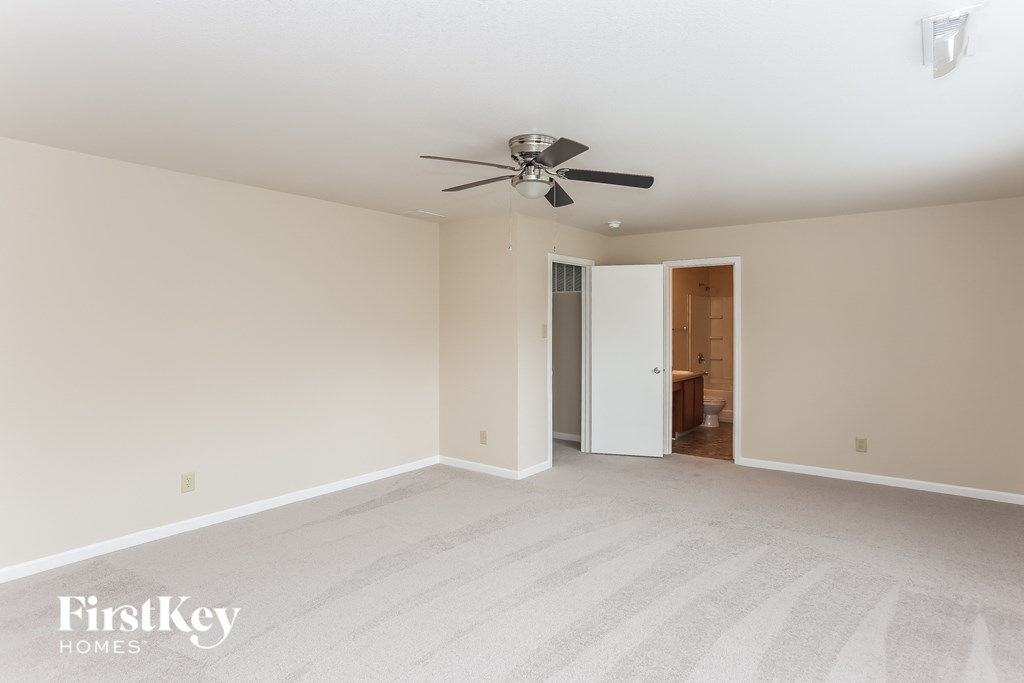 an empty living room with a ceiling fan and white carpet